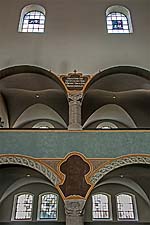 Kirchenraum der Erlöserkirche Schwabing - Detailansicht einer Stützenreihe an der Empore im Norden mit Steinmetzarbeiten an den Säulen und Wandmalereien.