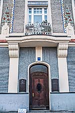 Detail Haus Leopoldstraße 77: Hauseingang (mit originaler Haustüre?) in der Straßenfassade und Balkon darüber mit Stuckornamenten.