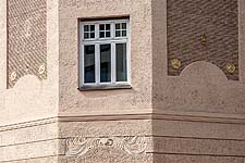 Detailausschnitt der Gebäudeecke mit Stuckornament, Putzfeldern und vergoldeten Stuckrosetten darin.
